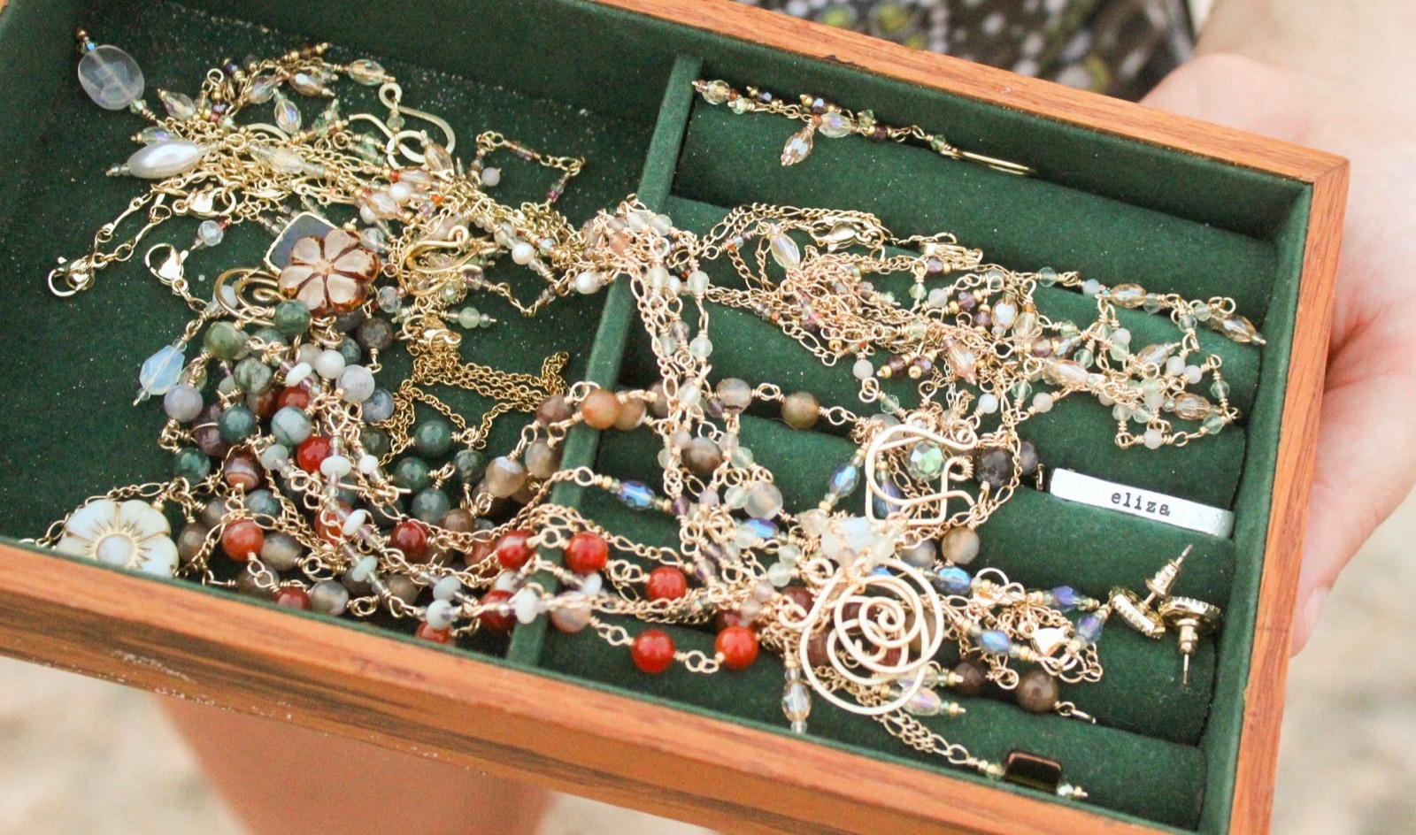 A hand holding open a green velvet jewelry box full of wire-wrapped gemstone chains